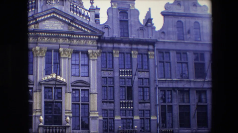 At the end of the zoom, the frame holds on Brussels architectural details including tall windows, columned trim, balcony elements, and adjacent historic frontage.