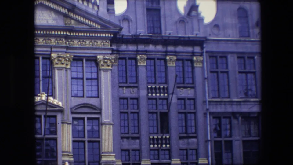 1967 Brussels frame with a closer view of an ornate historic building front, showing gold ornament, large windows, and upper facade details.