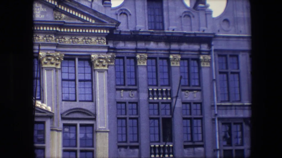 1967 Brussels home-movie frame showing ornate columns, multi-paned windows, gilded trim, and facade numerals reading 16 and 97.