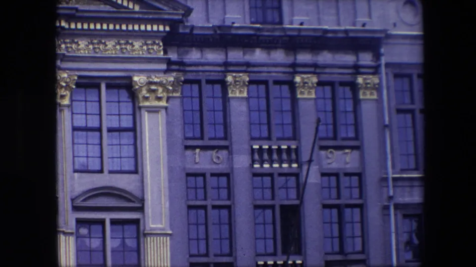 1967 Brussels frame showing the ornate historic facade with repeated window bays, gilded detailing, pale stone columns, and a narrow pole or flagstaff in front.