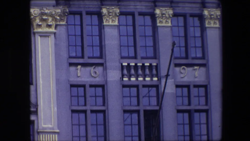 1967 Brussels 8mm frame showing a closer lower portion of a historic stone facade with multi-paned windows, ornamental capitals, vertical pilasters, and the numerals 16 and 97.