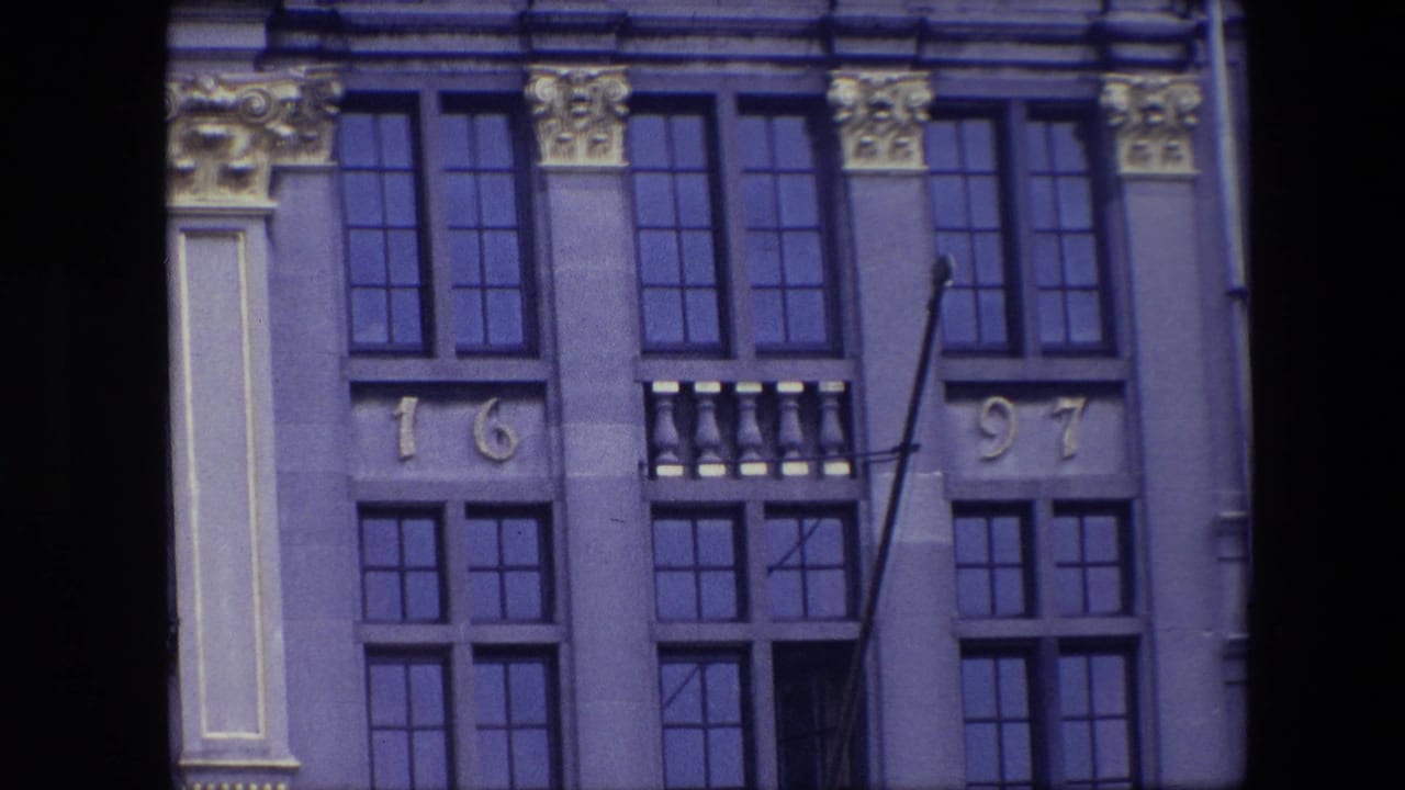 1967 Brussels footage frame with the facade centered on blue-tinted window panes, decorative gold capitals, and the visible 1697 numerals.