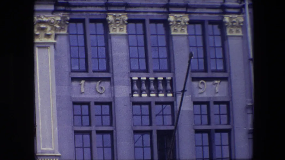 1967 Brussels footage frame with the facade centered on blue-tinted window panes, decorative gold capitals, and the visible 1697 numerals.