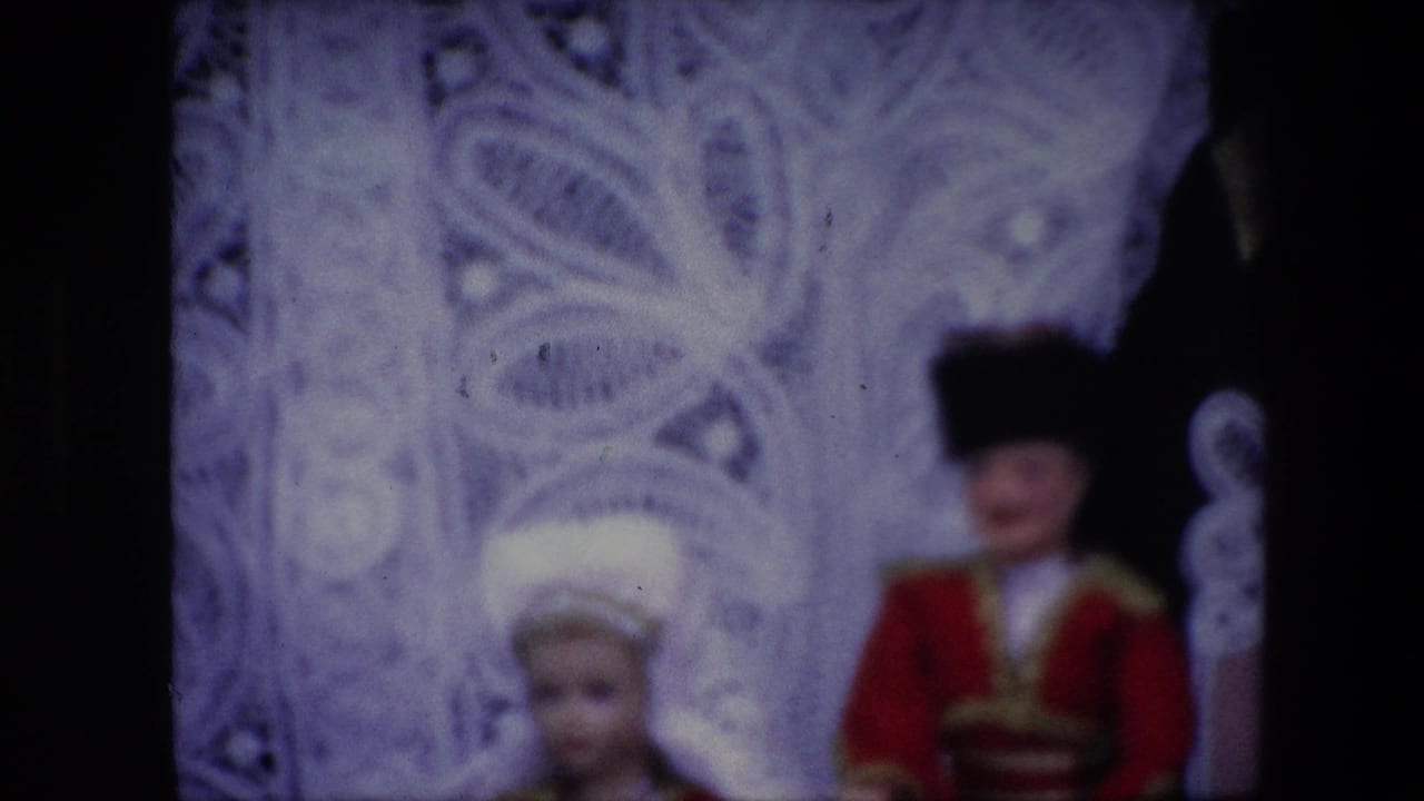 Two costumed dolls before a pale ornate filigreed backdrop.