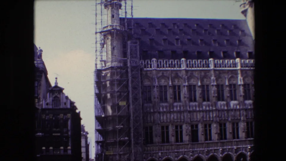 1967 Brussels home-movie frame showing a Gothic-style civic facade with scaffolding, arched ground-floor openings, tall windows, and a steep roofline.