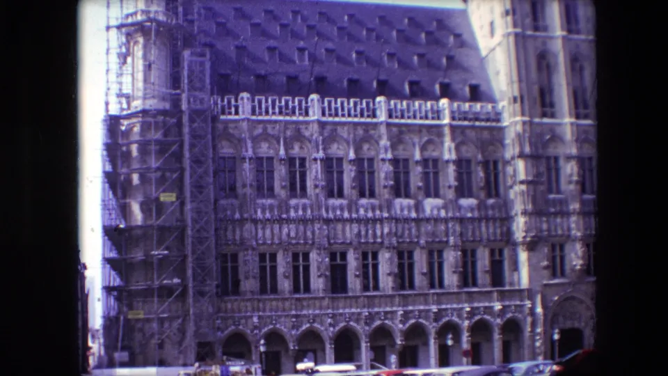 1967 Brussels 8mm frame showing the scaffolded historic facade with tall windows, arched ground-level openings, and part of a neighboring doorway at right.