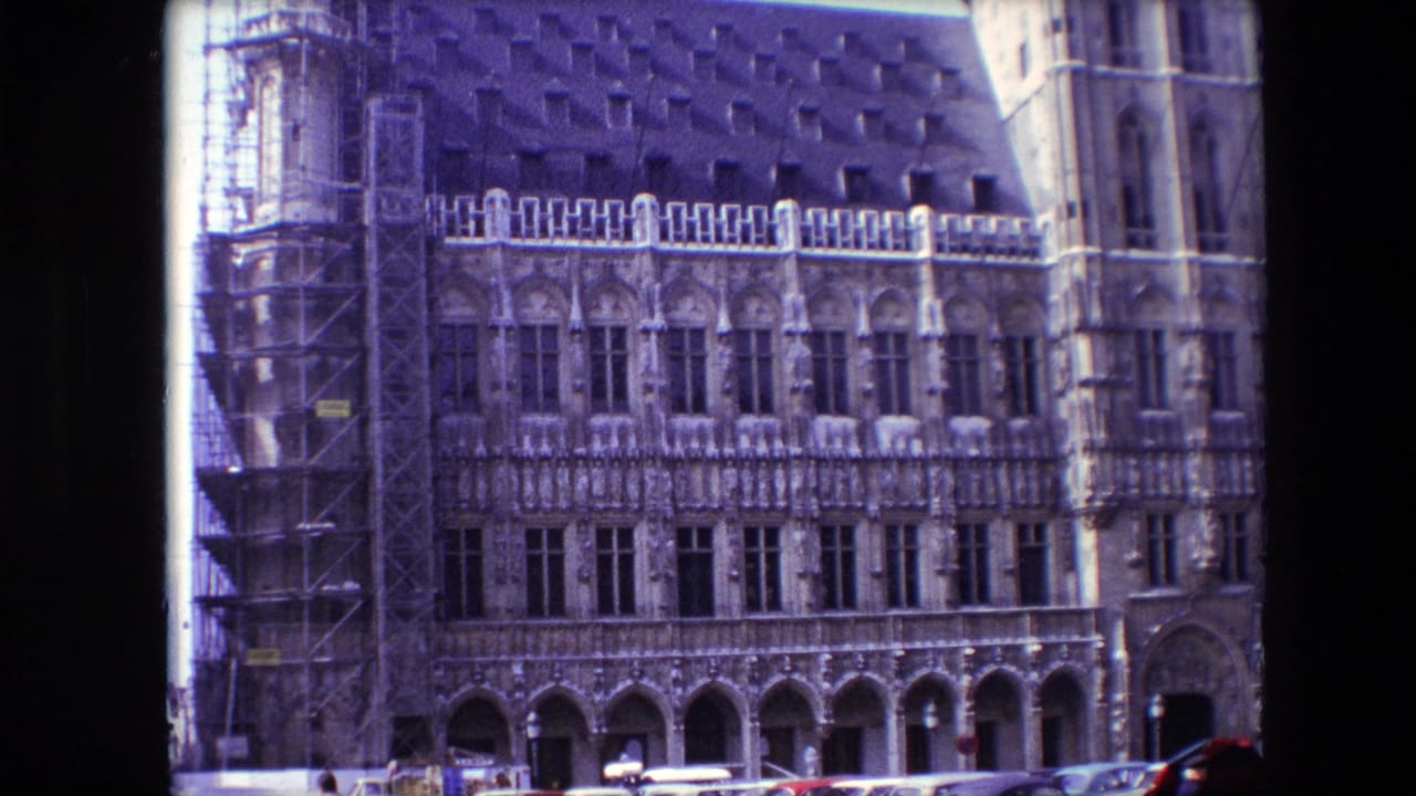 1967 Brussels home-movie frame showing an ornate Gothic building facade with restoration scaffolding on the left and cars parked or moving below.