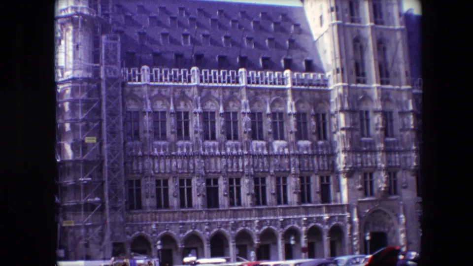 1967 Brussels frame of a historic Gothic facade, showing scaffolding at the left edge, a vertical tower section at the right, and classic cars along the lower street.