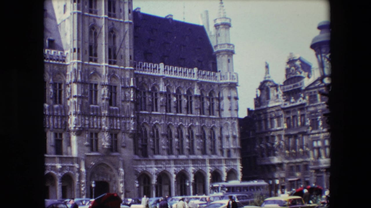 Ornate Gothic building frontage with a bus, cars, pedestrians, and a lamp post in the foreground.