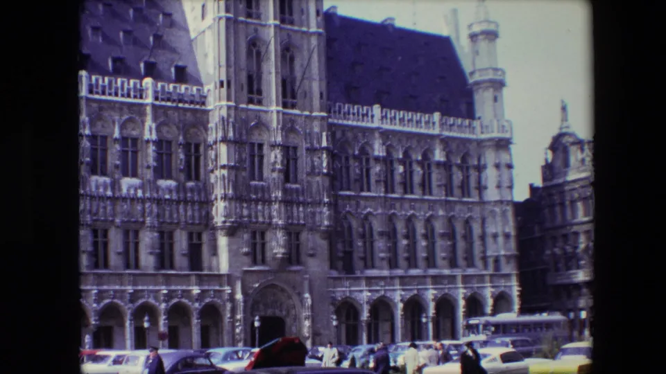 1967 Brussels frame capturing the Town Hall facade and tower details above a street lined with cars, yellow taxis, pedestrians, and a bus in the foreground.