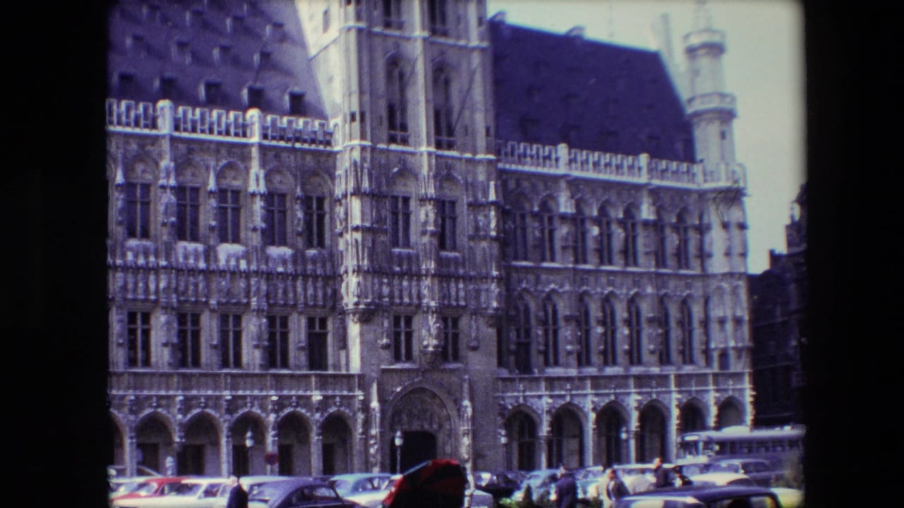 Ornate Gothic-style building facade with parked cars and a few pedestrians in front.