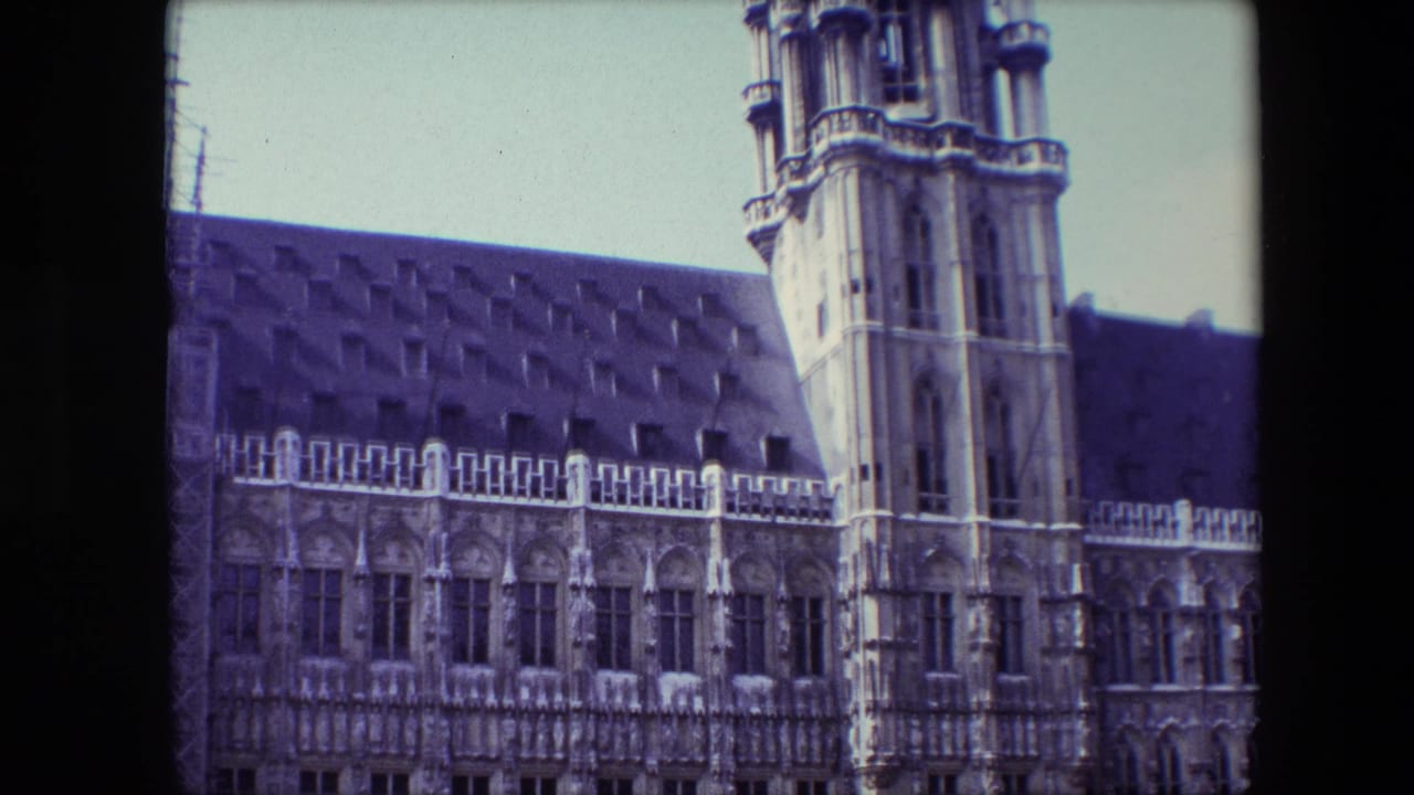 1967 Brussels frame with the visitor camera tilted upward toward a tall stone tower, arched facade windows, and a dark roofline.