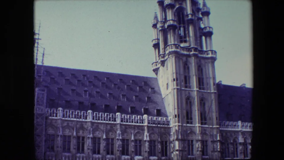 1967 Brussels home-movie frame showing the tower cropped higher in the composition beside a Gothic-style facade and dark tiled roof.