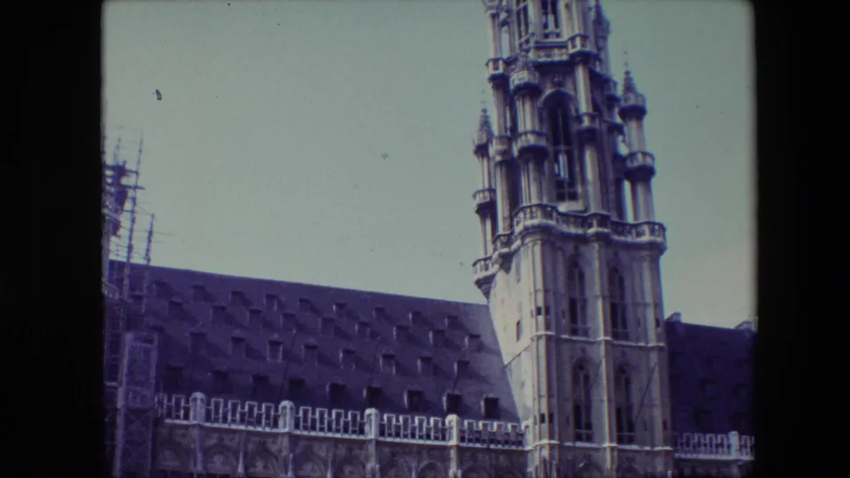 Final 1967 Brussels frame looking up at the upper section of a stone tower above the decorative roofline of a Gothic-style building.