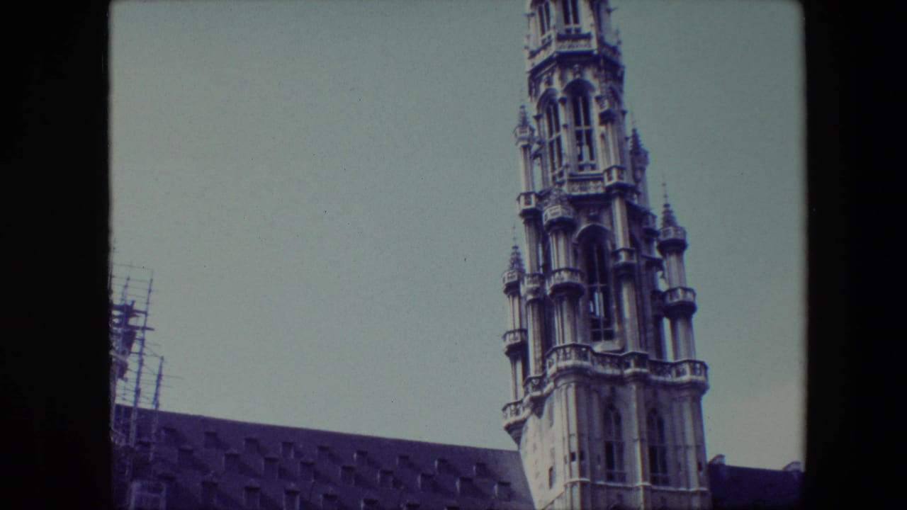 Upper Gothic tower beside a long roofline under a pale sky.