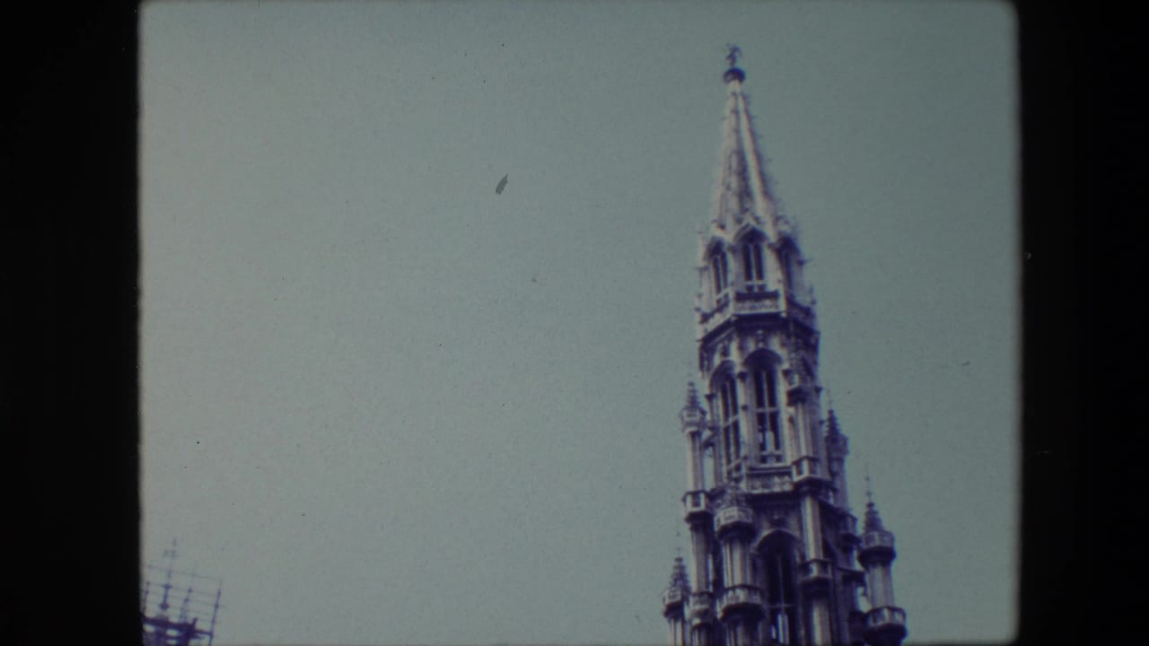 Low-angle 1967 Brussels home-movie frame showing the upper portion of an ornate Gothic-style spire against a pale blue sky.