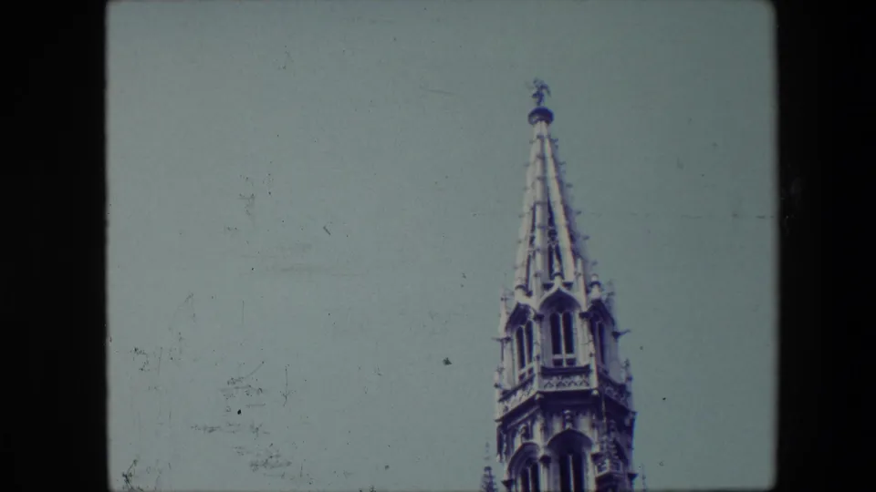 Low-angle 8mm frame from Brussels in 1967 showing the ornate tower top below a broad area of pale sky.