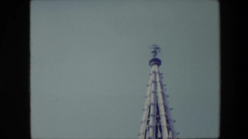 1967 Brussels frame with the upper steeple shifted lower in view, showing pointed stonework and a small figure at the top against open sky.