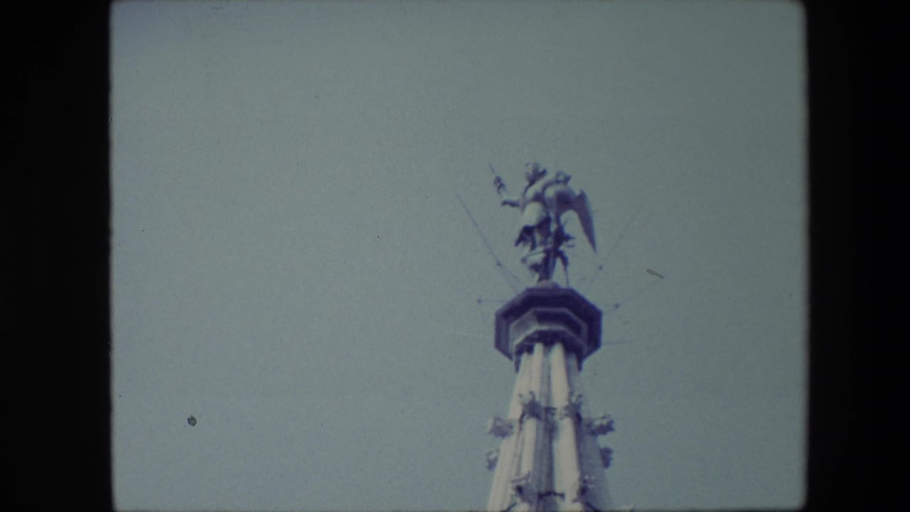 The Brussels spire remains framed from below, with the winged figure at the summit silhouetted softly against the grey sky.