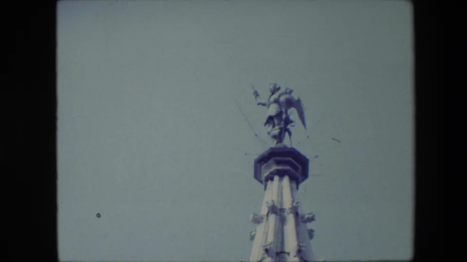 The Brussels spire remains framed from below, with the winged figure at the summit silhouetted softly against the grey sky.