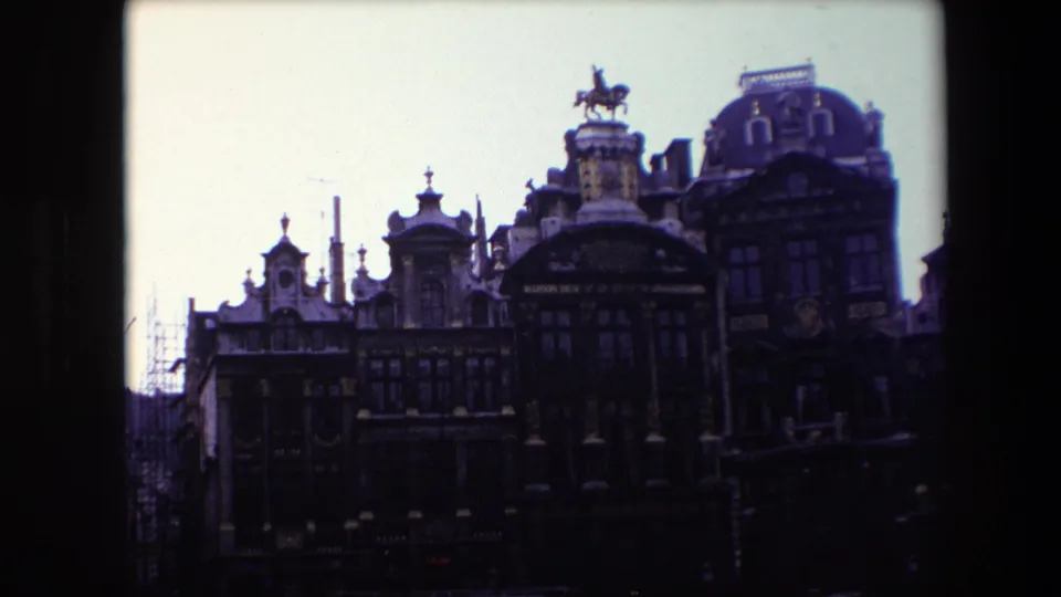 1967 Brussels 8mm frame showing ornate historic facades with rooftop statuary, dormer windows, and darkened street-level architecture.
