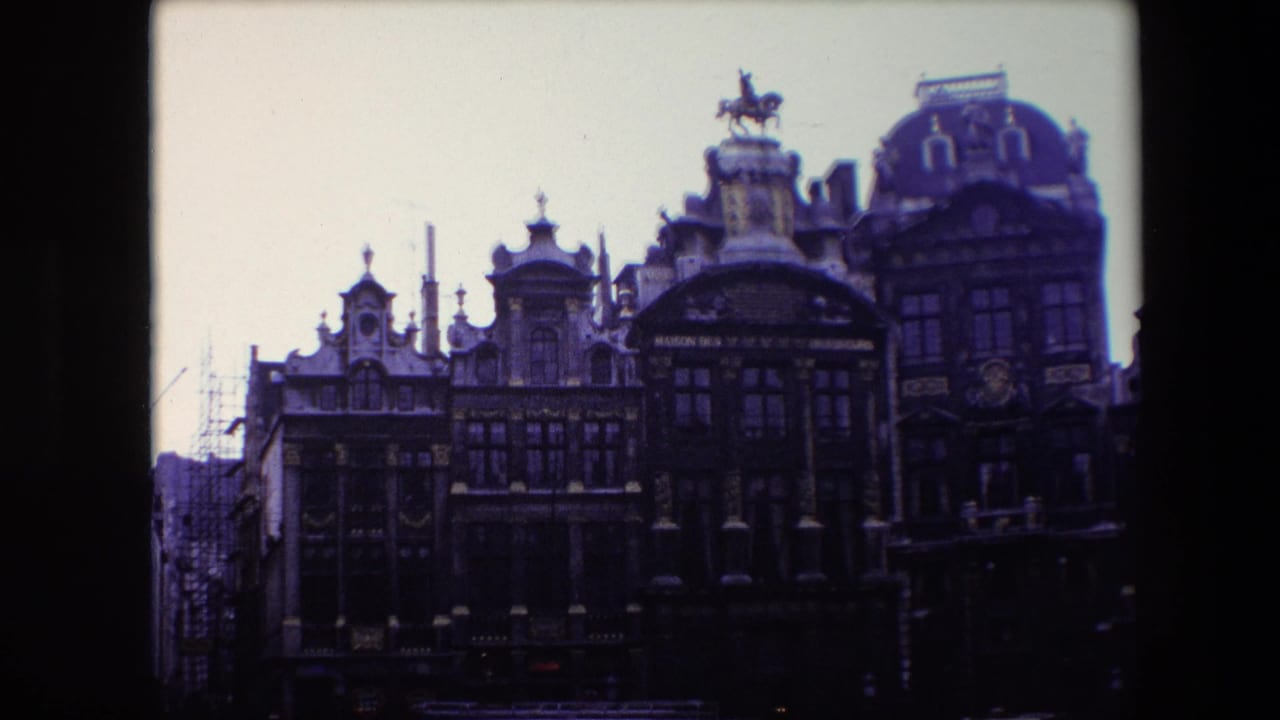 1967 Brussels 8mm frame showing an ornate historic facade with multiple gables, tall windows, gold-toned trim, street lamps, and an equestrian statue above the roofline.