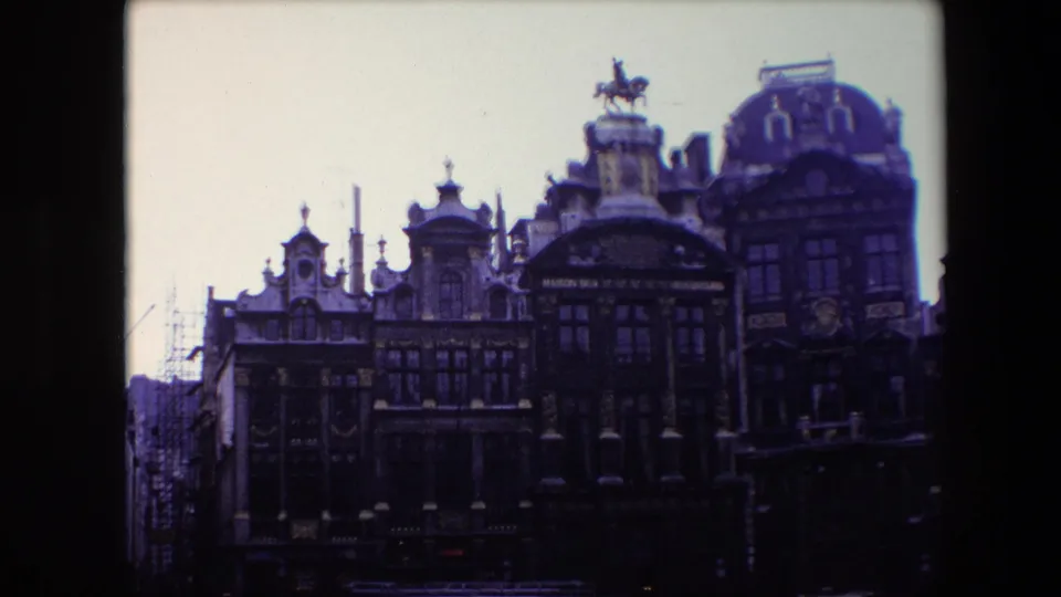 1967 Brussels 8mm frame showing an ornate historic facade with multiple gables, tall windows, gold-toned trim, street lamps, and an equestrian statue above the roofline.