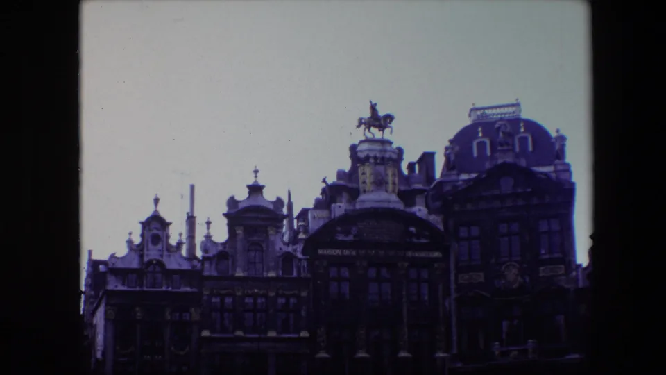 Final 1967 Brussels frame with the camera framed slightly lower, keeping the ornate roofline, central arched facade, windows, and rooftop equestrian statue in view.