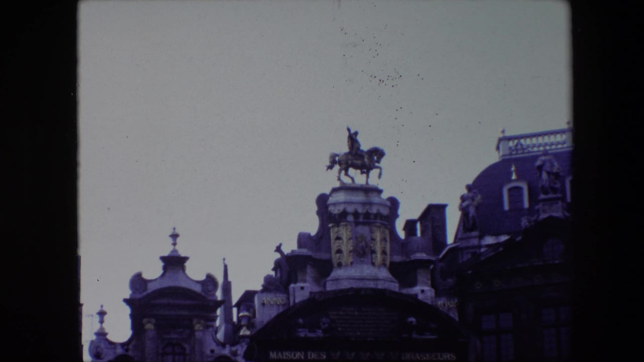 The camera frames the rooftop equestrian statue and adjacent ornate Grand Place rooflines in Brussels, with soft 8mm color and visible film border.
