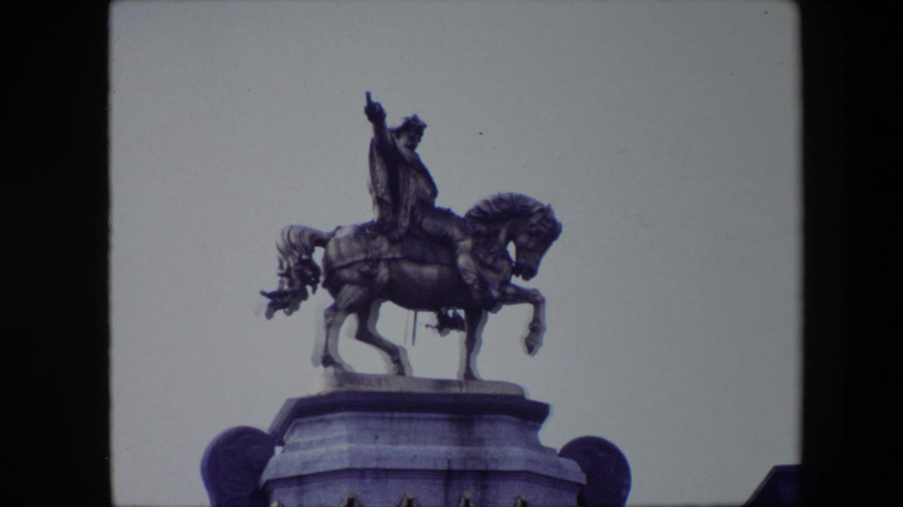 Closer 1967 Brussels frame of a bronze rider on horseback above a stone pedestal, filmed from below against an overcast sky.