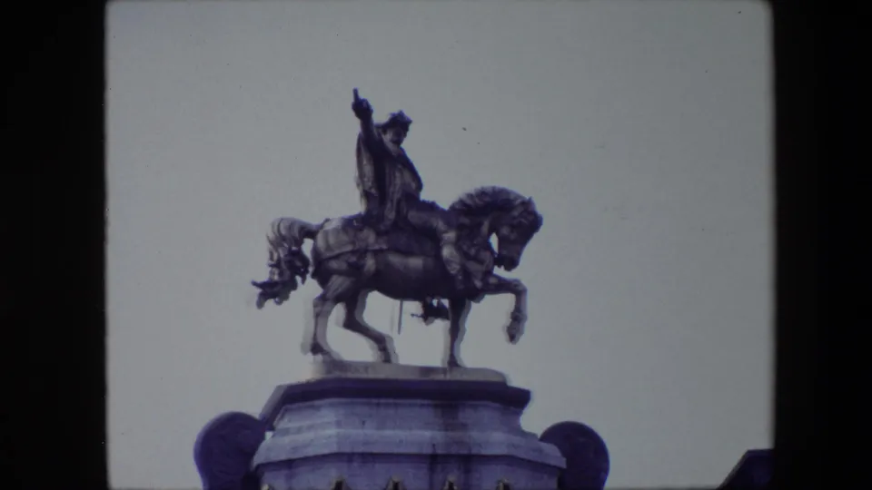 Closer 1967 Brussels frame of a bronze rider on horseback above a stone pedestal, filmed from below against an overcast sky.