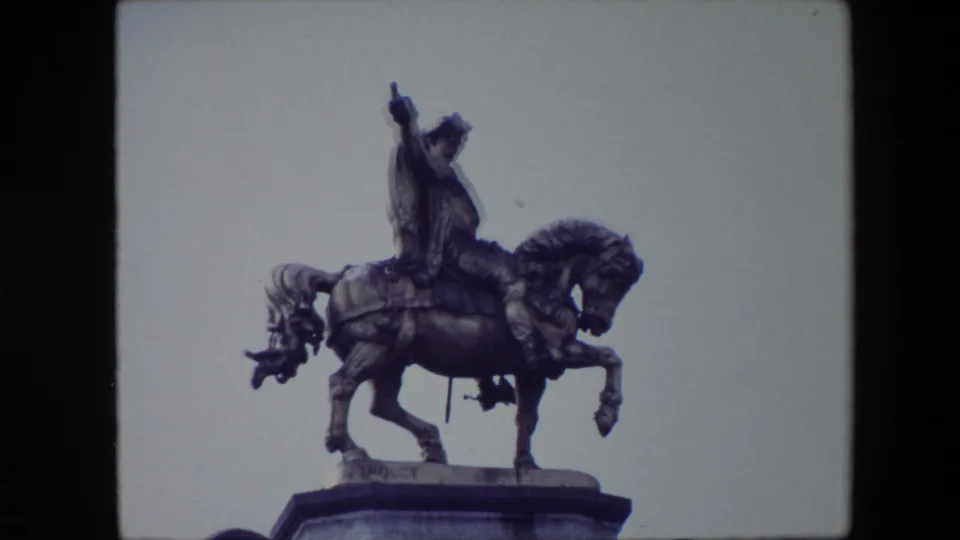 Close 8mm frame from Brussels in 1967 showing the equestrian statue larger in view, with the horse body, raised foreleg, rider, and pedestal top visible.