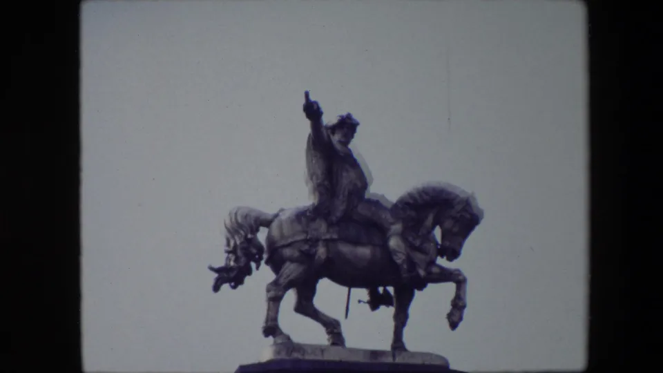 An equestrian monument in Brussels, Belgium, filmed in 1967 from a low visitor viewpoint against a pale sky with 8mm grain and soft color.