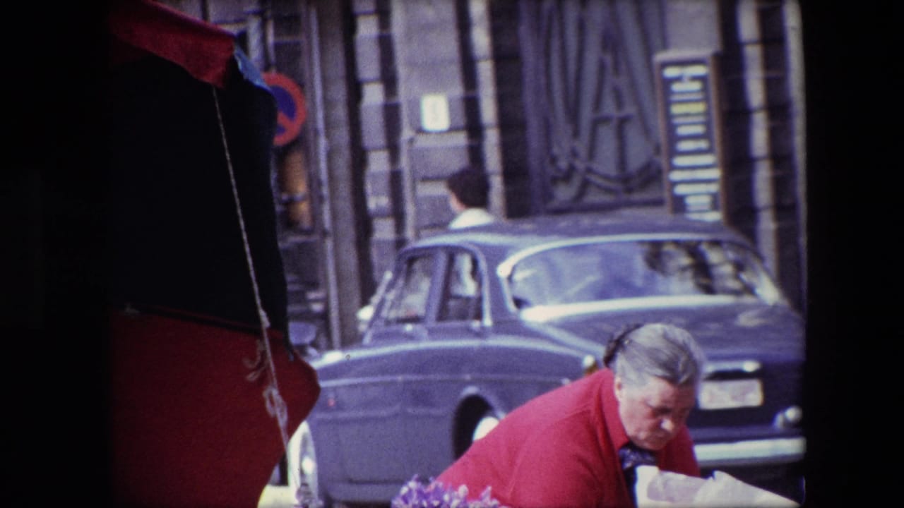 The 1967 Brussels street scene shows the woman in a red coat bent toward goods or bags at the stall, with the red-and-black umbrella, ornate building facade, and vintage blue sedan visible nearby.