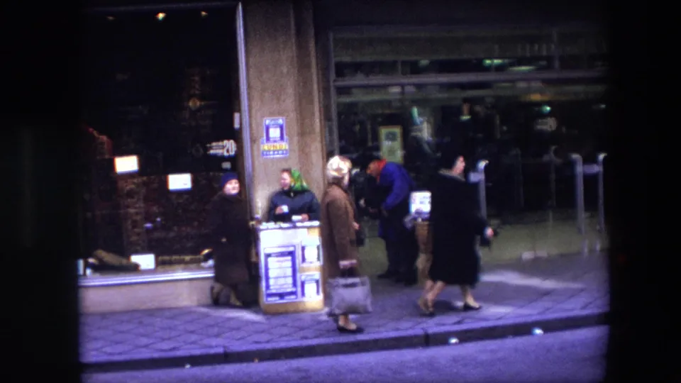 Several adults in coats stand or walk near a Brussels storefront while the donkey with its basket display remains at the sidewalk edge.