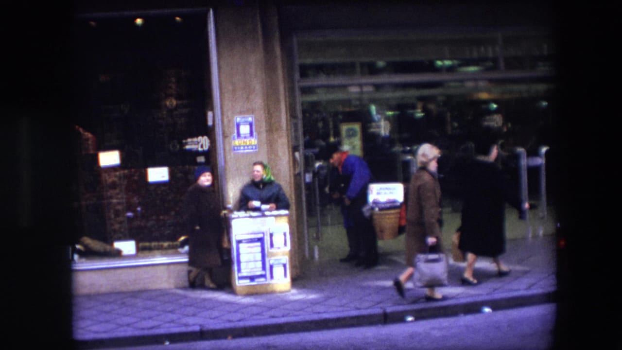 1967 Brussels sidewalk scene showing pedestrians passing glass storefront doors and two small stand-like selling points under artificial light.