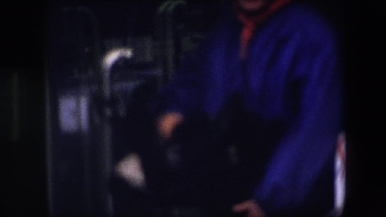 Blue-jacketed person partly cropped while moving or gesturing in a dim interior.