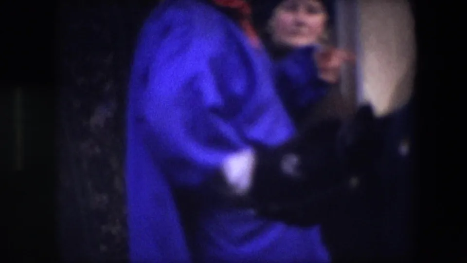 A person in a bright blue jacket stands near another visible face at the right edge of the frame, suggesting a brief interaction inside the 1967 Brussels interior scene.