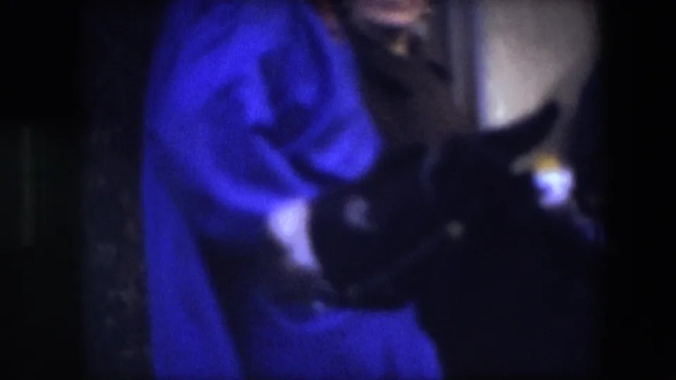 At the end of the 1967 Brussels clip, the woman in blue remains close to the dark-clad person, with the handheld 8mm frame emphasizing gesture, proximity, and low-light color texture.
