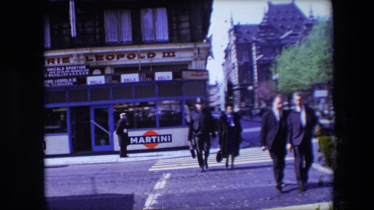 In Calais, France, in 1967, adults in coats and suits cross a zebra crossing toward the camera with storefront signage and Martini advertising behind them.