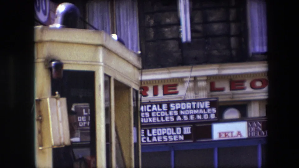 1967 Calais storefront view with partial brasserie lettering, French signage, a yellow streetcar or vehicle edge, upper windows, and dark vertical obstructions.