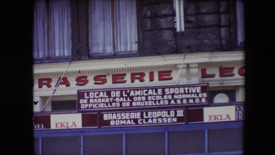 1967 Calais brasserie facade with readable French sign text, EKLA advertising, red storefront lettering, upper windows, and dark vertical obstructions crossing the view.