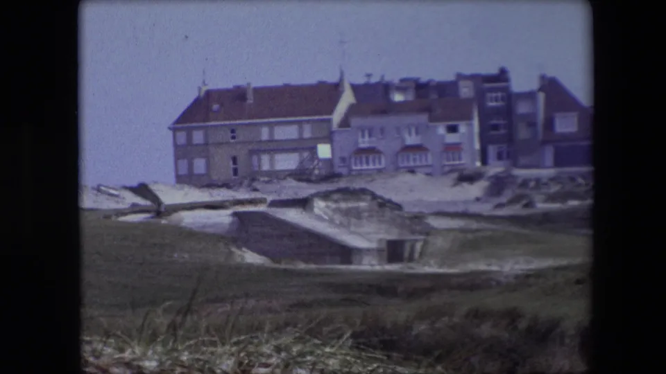 1967 Calais 8mm frame showing a weathered coastal building, sandy terrain, grass, and a low concrete structure in front.