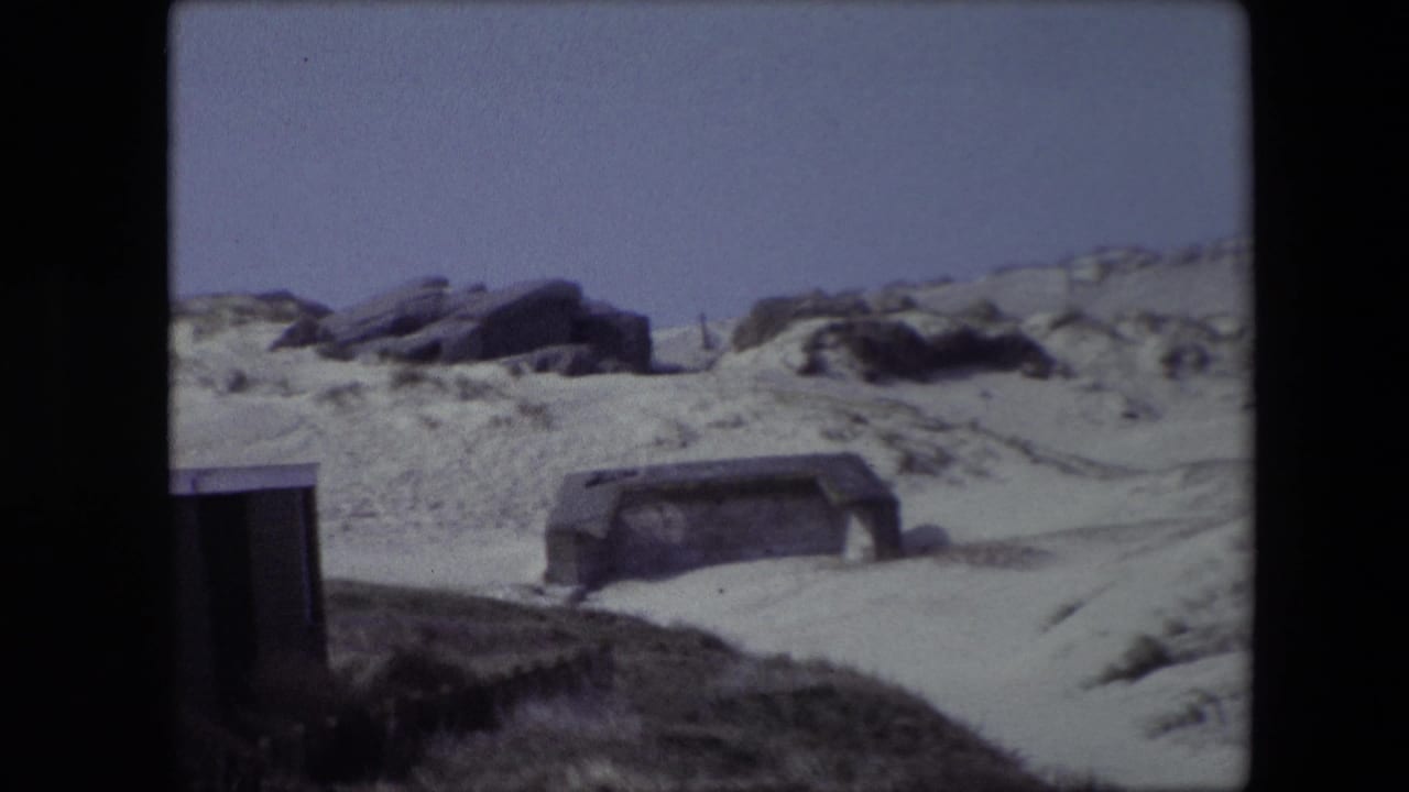 Partly buried concrete structure in sandy dunes with rocks along the ridge.