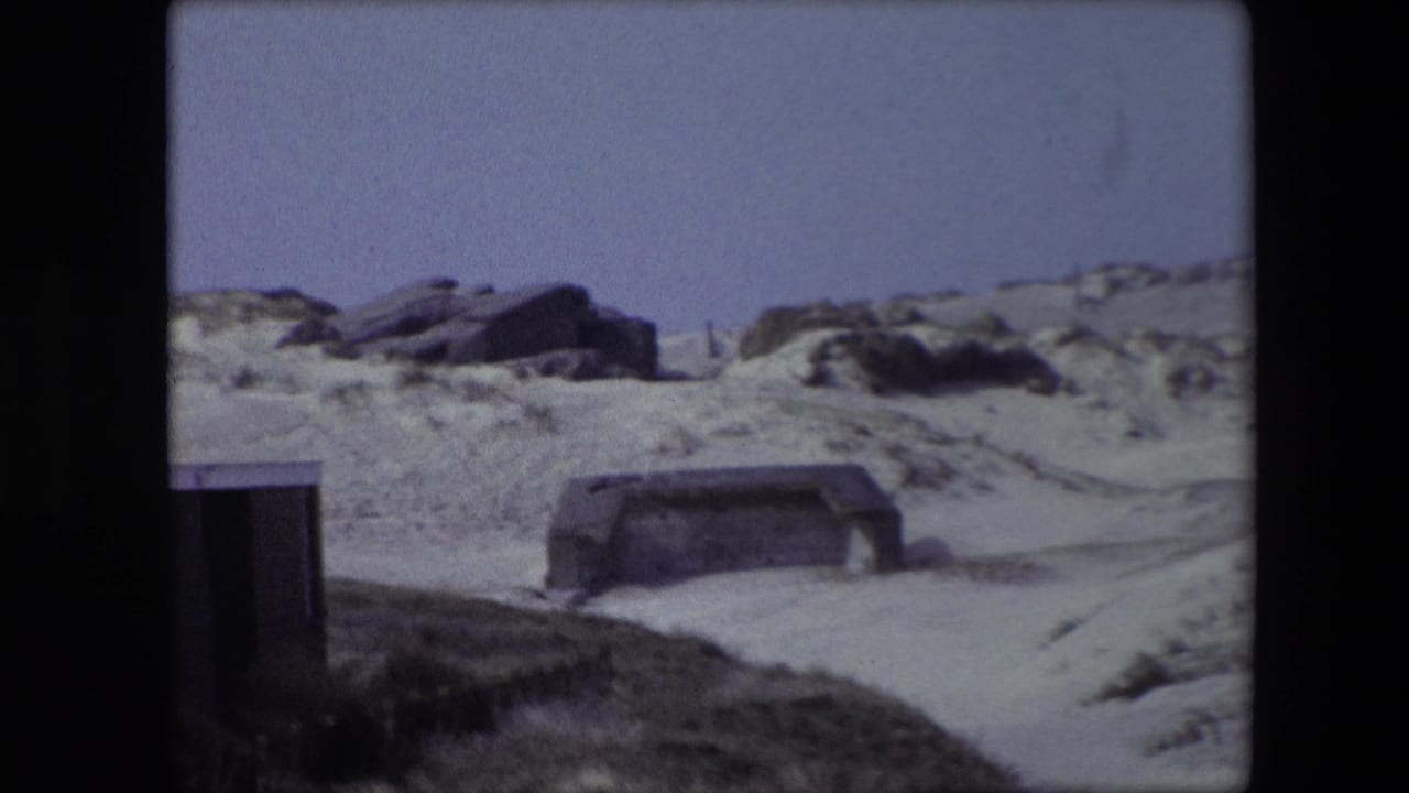 1967 Calais-area 8mm frame showing weathered concrete bunker forms set into sandy coastal dunes beneath a washed-out sky.