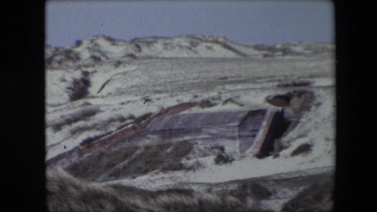 Sloped concrete bunker entrance emerging from wind-shaped dunes.