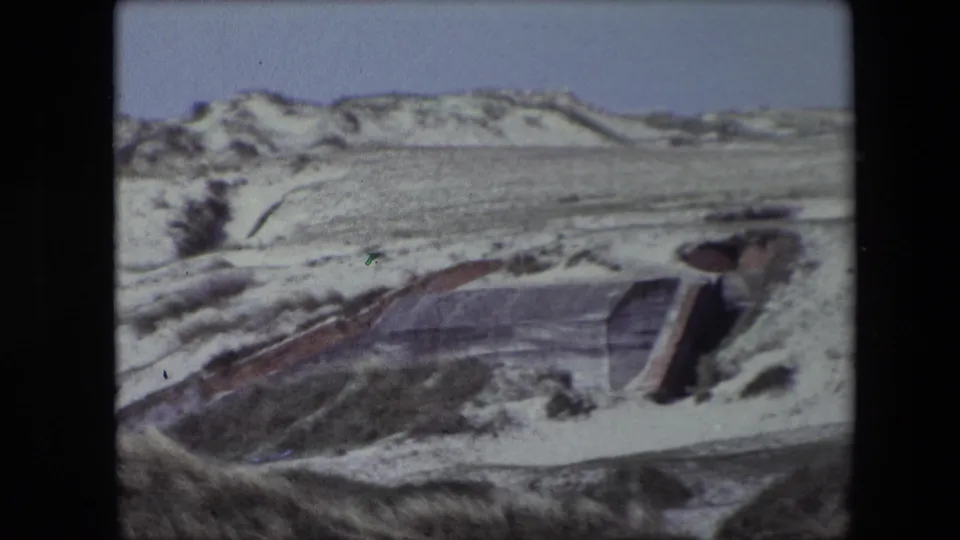Weathered concrete bunker entrance appears partly exposed in the sandy dunes near Calais, France, in a faded 1967 8mm home-movie frame.