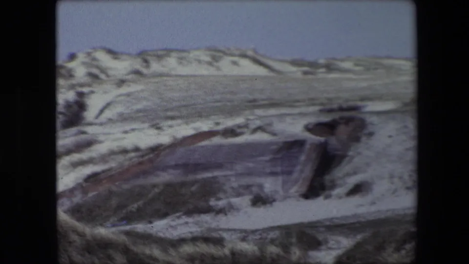 Final 1967 Calais 8mm frame showing low concrete bunker remains in a quiet sandy dune landscape with no people visible.