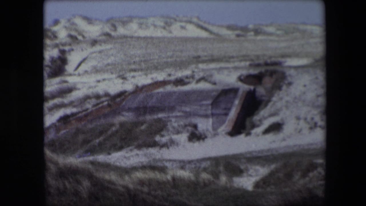 Low concrete structure partly surrounded by pale dunes and sparse vegetation.