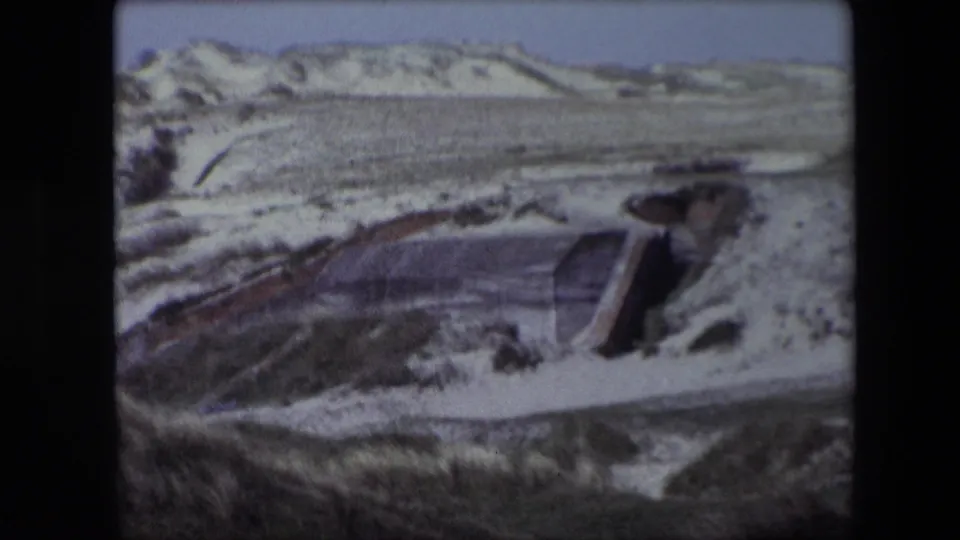 1967 Calais frame with a bunker-like concrete form set into pale dunes, with sparse vegetation and low ridges in the distance.